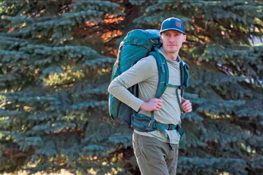 a man wearing a backpack stands in front of a tree