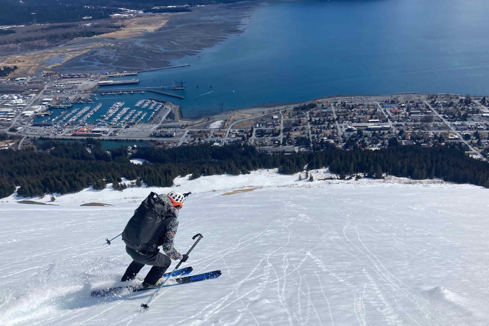 A man skis down a slope above a small town along the ocean.