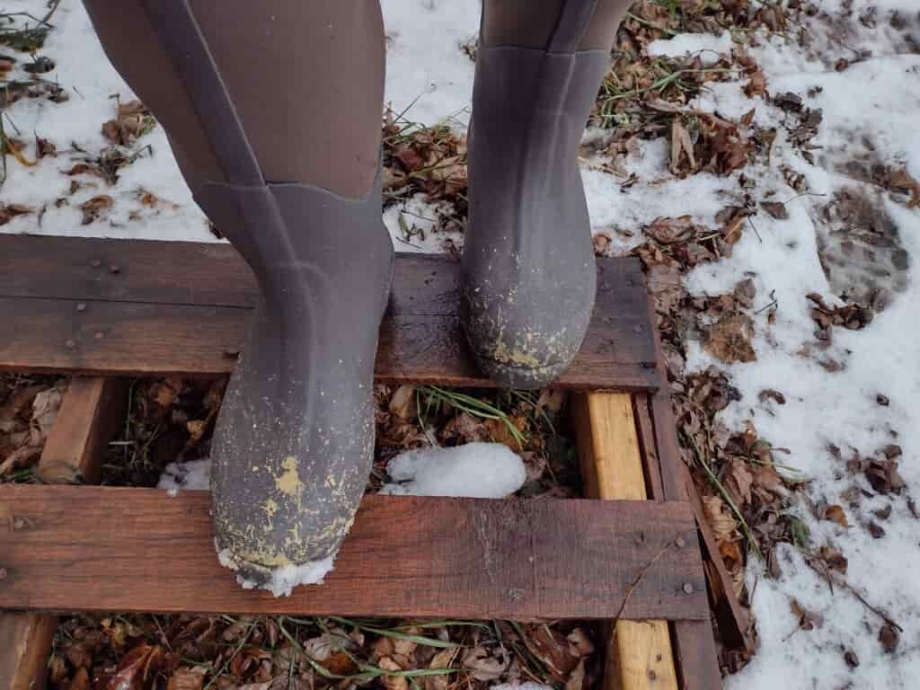 Ground level view of someone wearing the brown Original Muck Boot Wetland standing on a pallet.