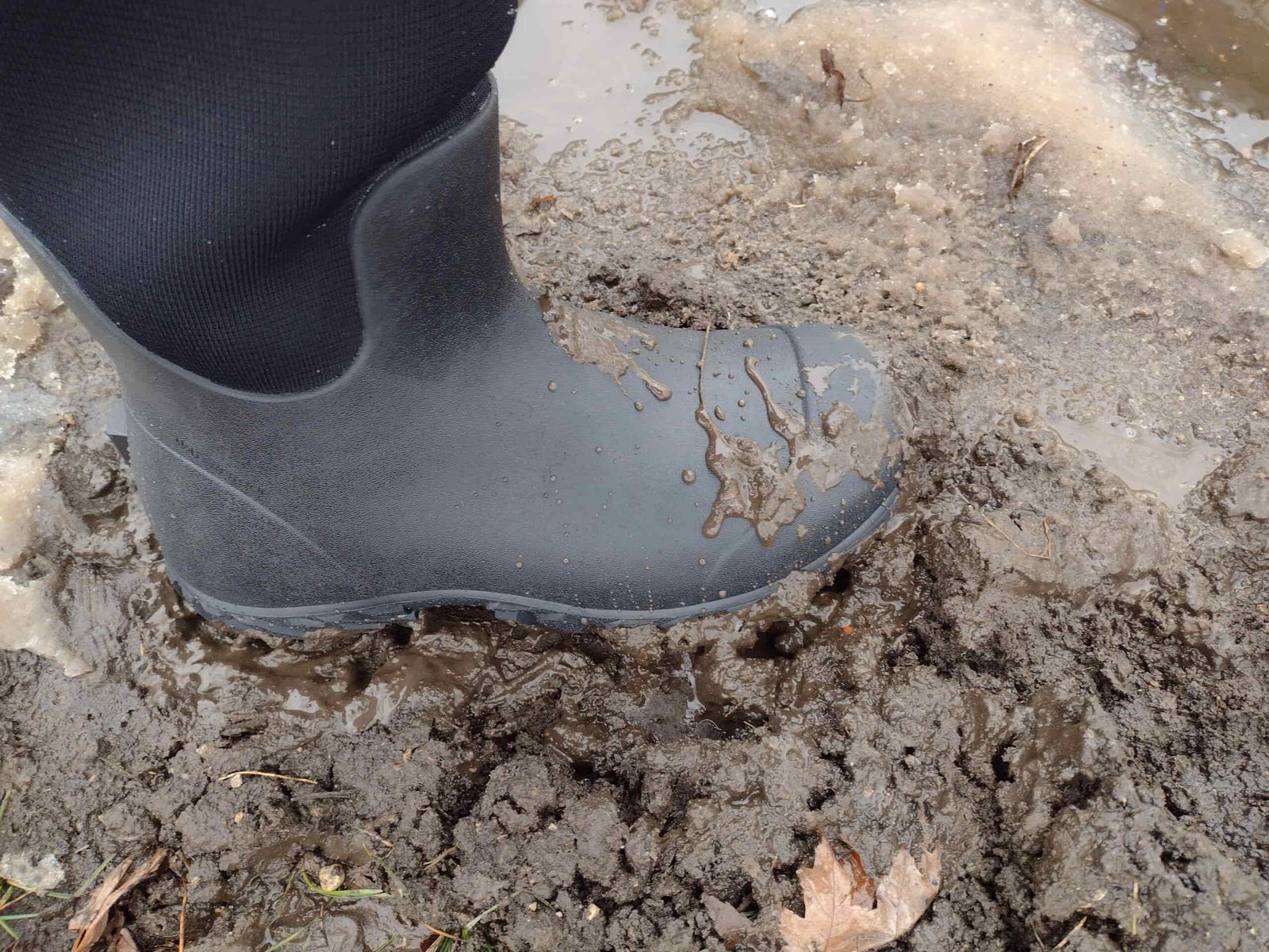 Ground level view of someone wearing the black Bogs Workman in muddy snow and water.