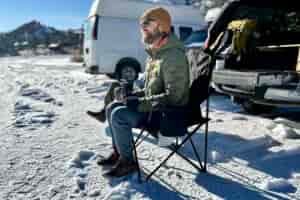 A man sits in a camping chair in a snowy parking lot.