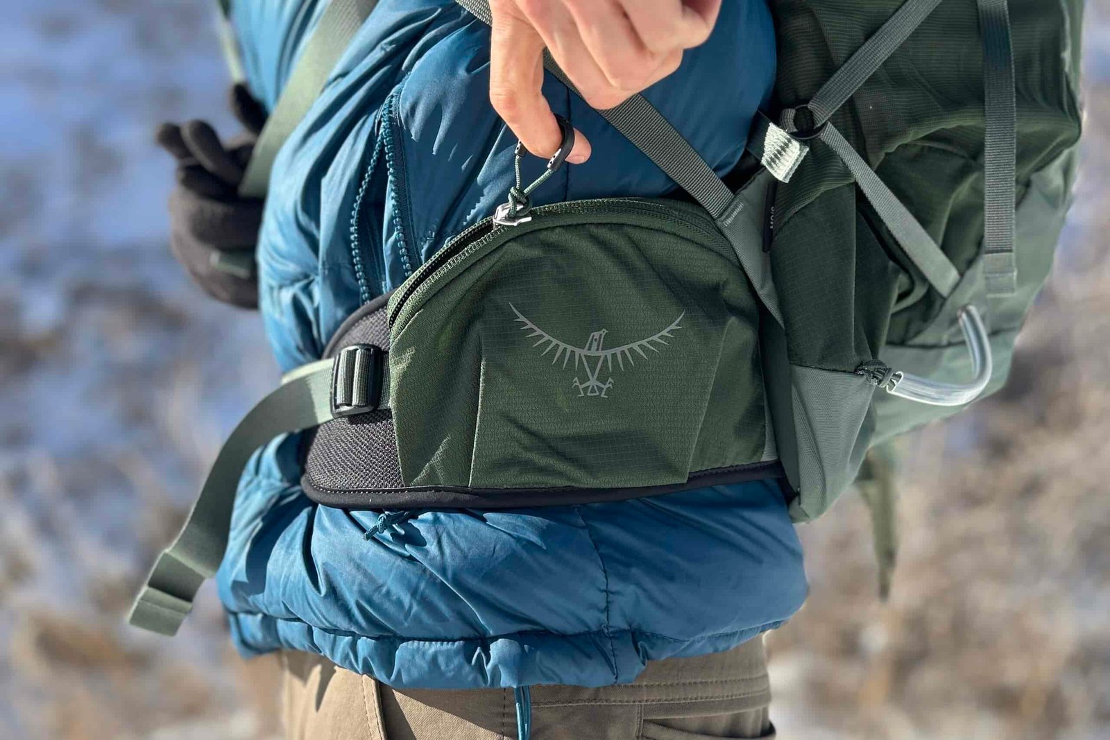 Close up of a person unzipping the wide waist strap pockets of a daypack.