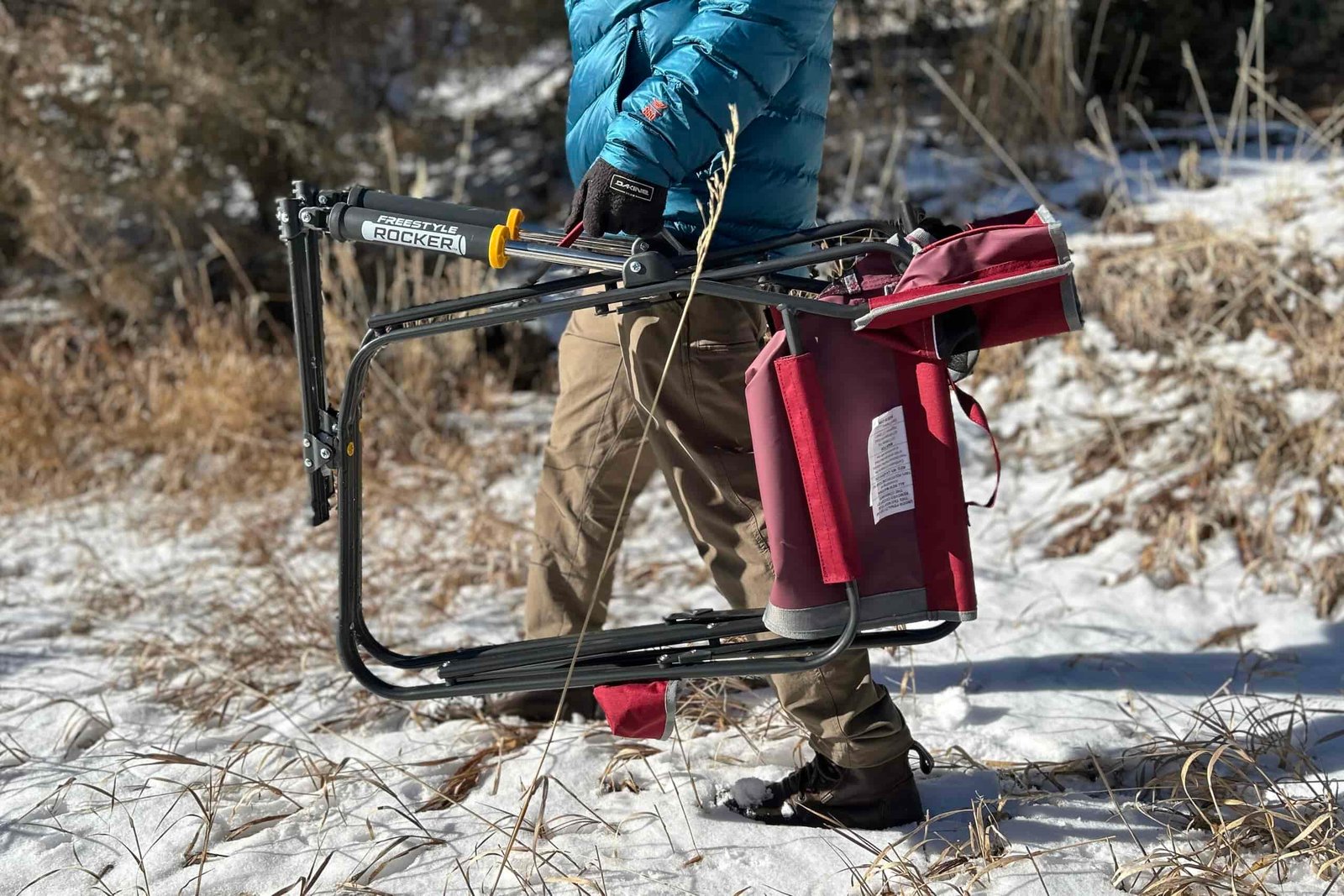 Close up of a person carrying a camping chair sideways through a snowy forest.