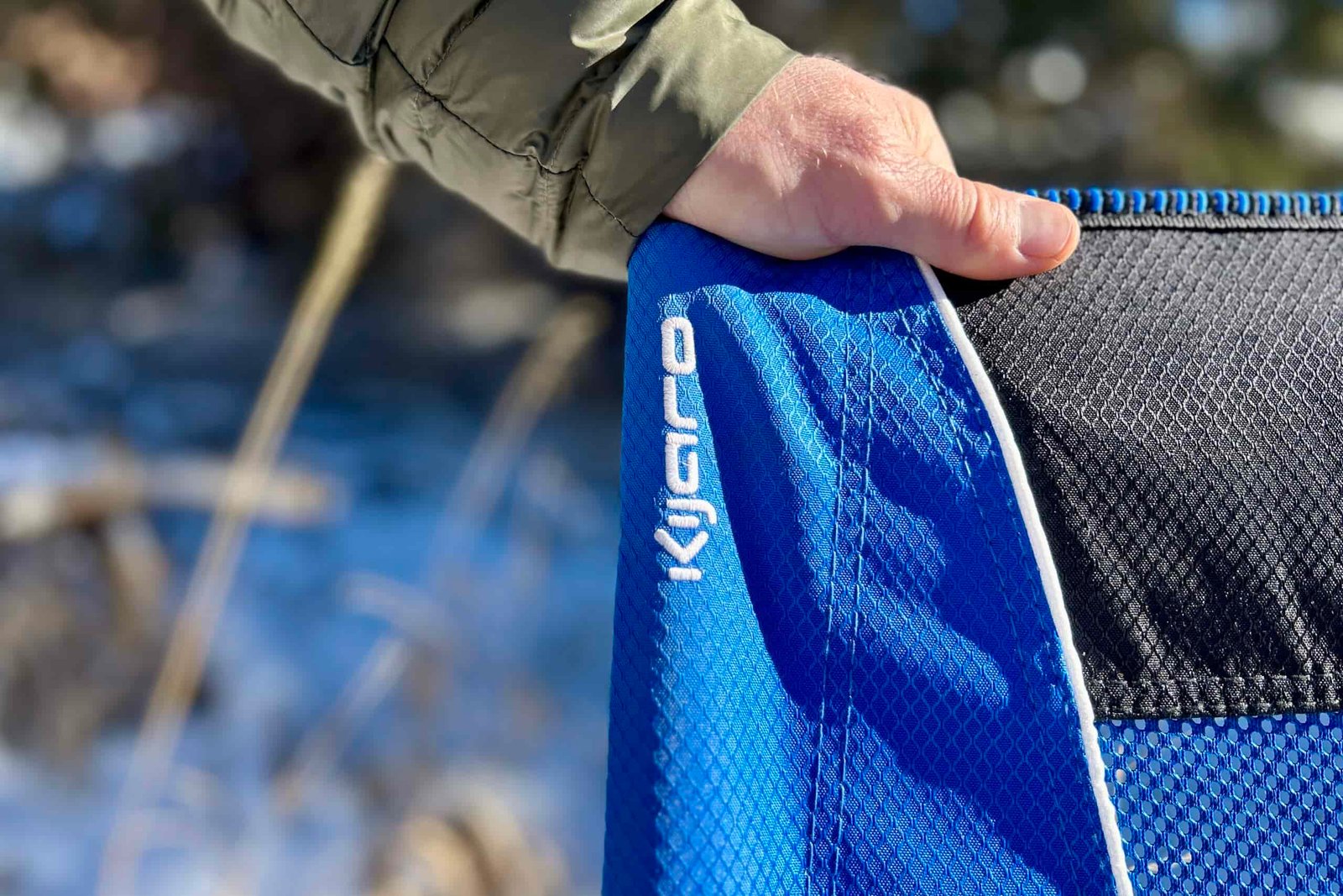Close up of a person's hand on the backrest of a camping chair with the logo visible.