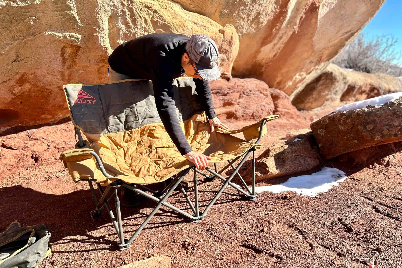 A man sets up a two person camping chair in a desert place.
