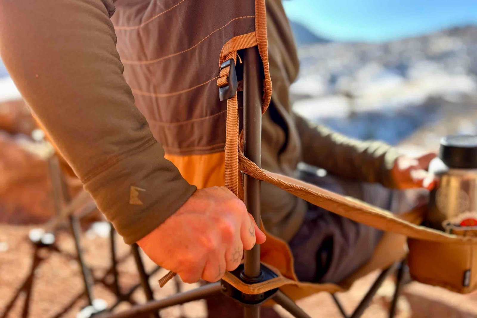 A person tightens the adjustable nylon strap of the armrest on a camping chair.