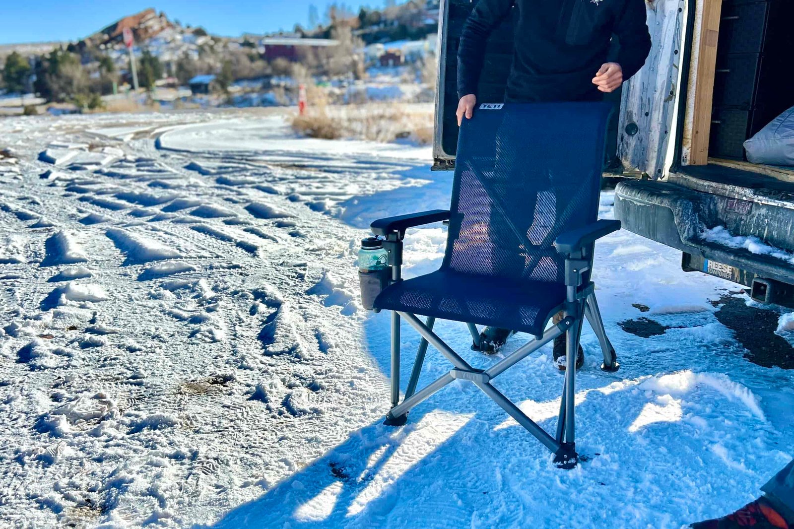 A person holds onto the back of a camping chair in a parking lot.