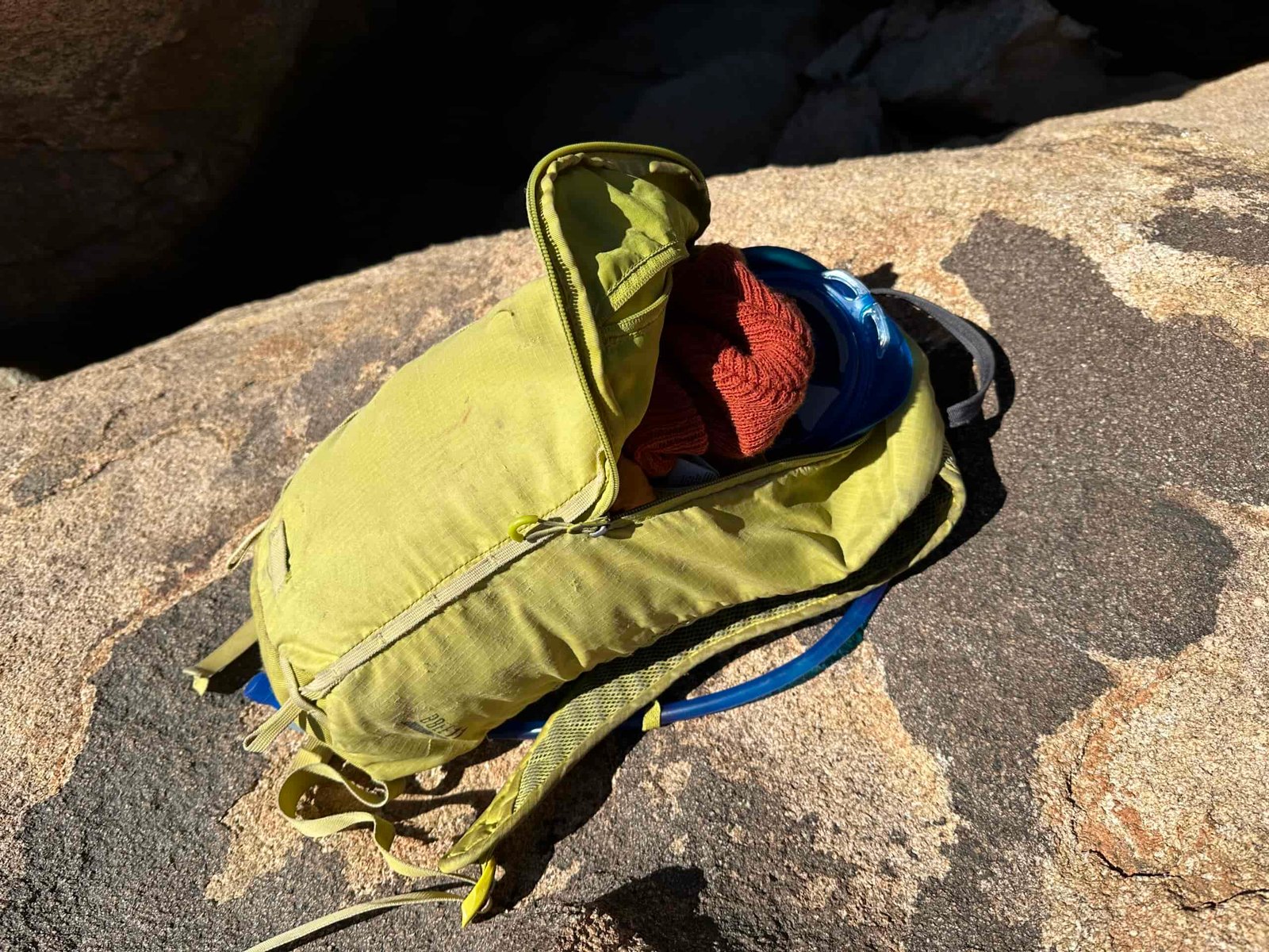 A close up photo of the CamelBak Crux tucked into the hydration sleeve of a small yellow daypack that's sitting on a large granite rock.