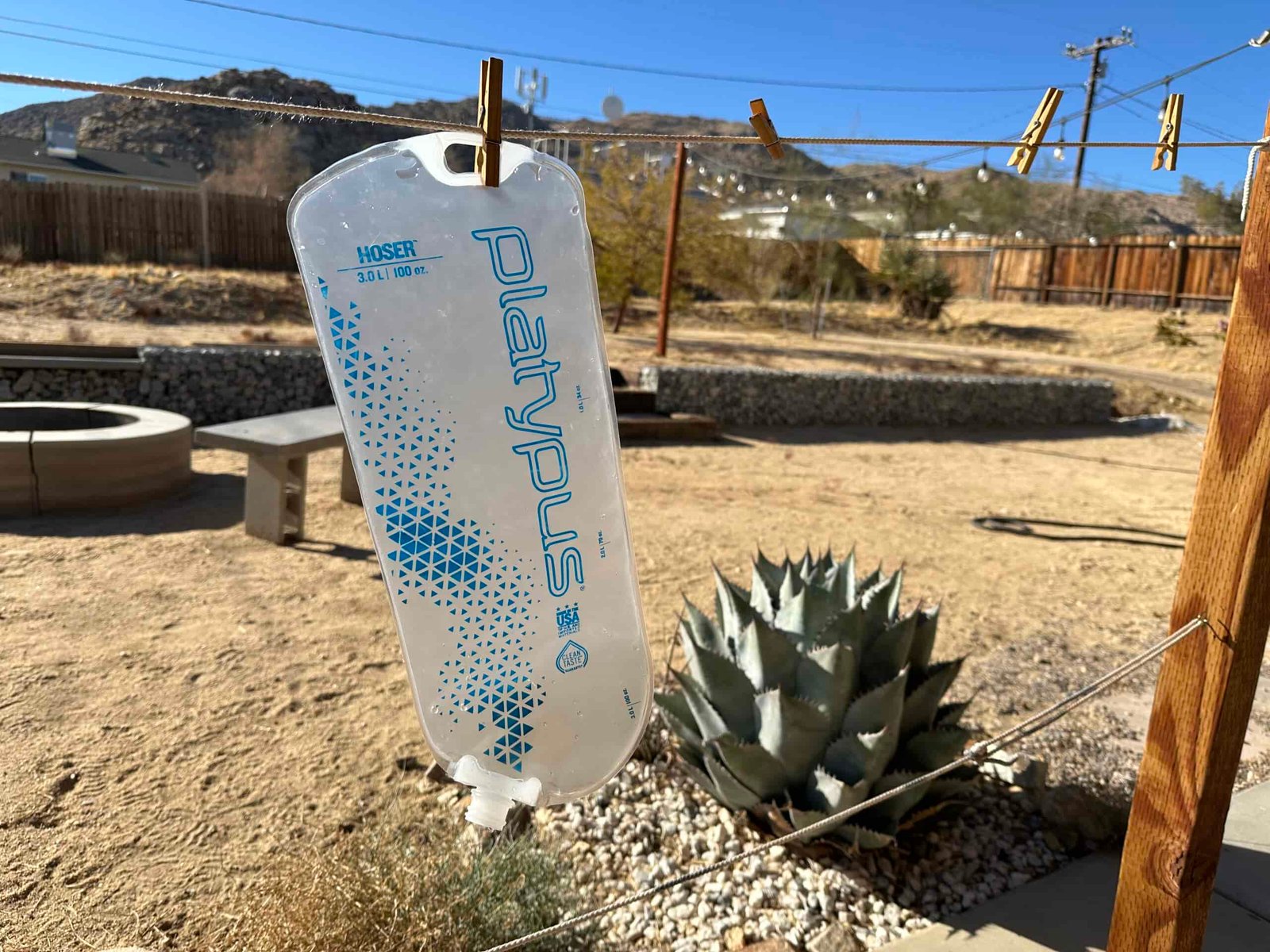 Image showing the Platypus Hoser Reservoir hanging to dry on a clothesline. The background is a backyard in the desert.