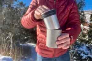 A hiker nests the two pieces of the insulated mug together with a snowy background.