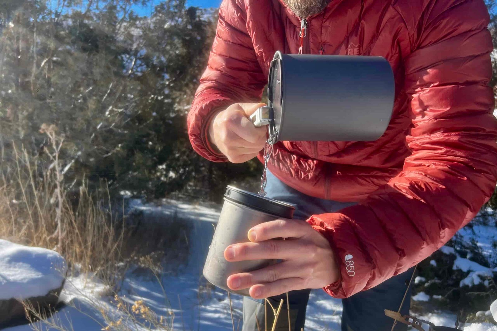 A hiker pours water from the pot into the insulated mug of the soto thermostack combo against a snowy desert background.