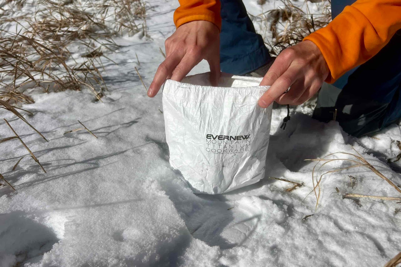 A hiker holds open the stuff sack of the evernew pasta pot against a snowy background.