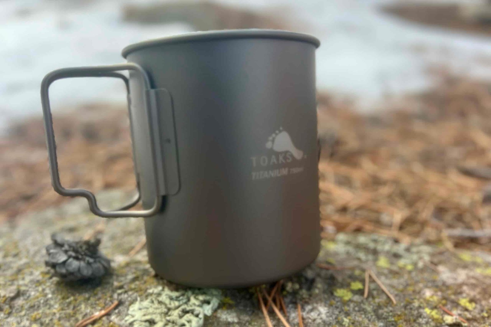 A titanium cook pot sits on a rock.