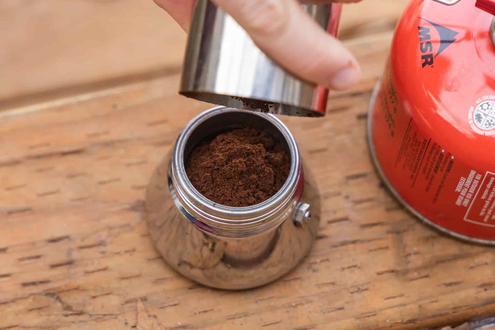 A hand dumps coffee into the coffee basket of the GSI Mini Espresso.
