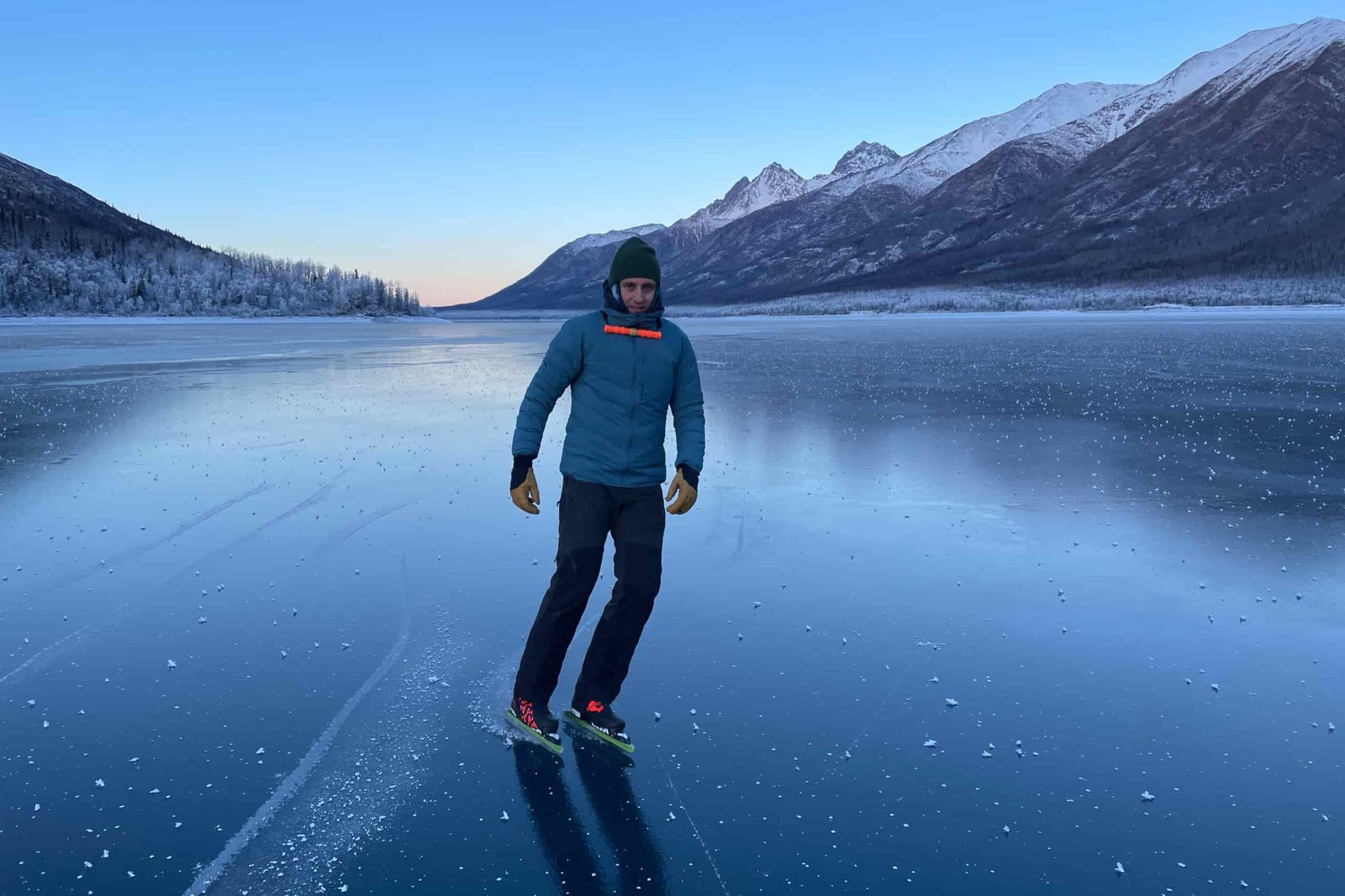 A man ice skates on a blue ice lake wearing a blue jacket.