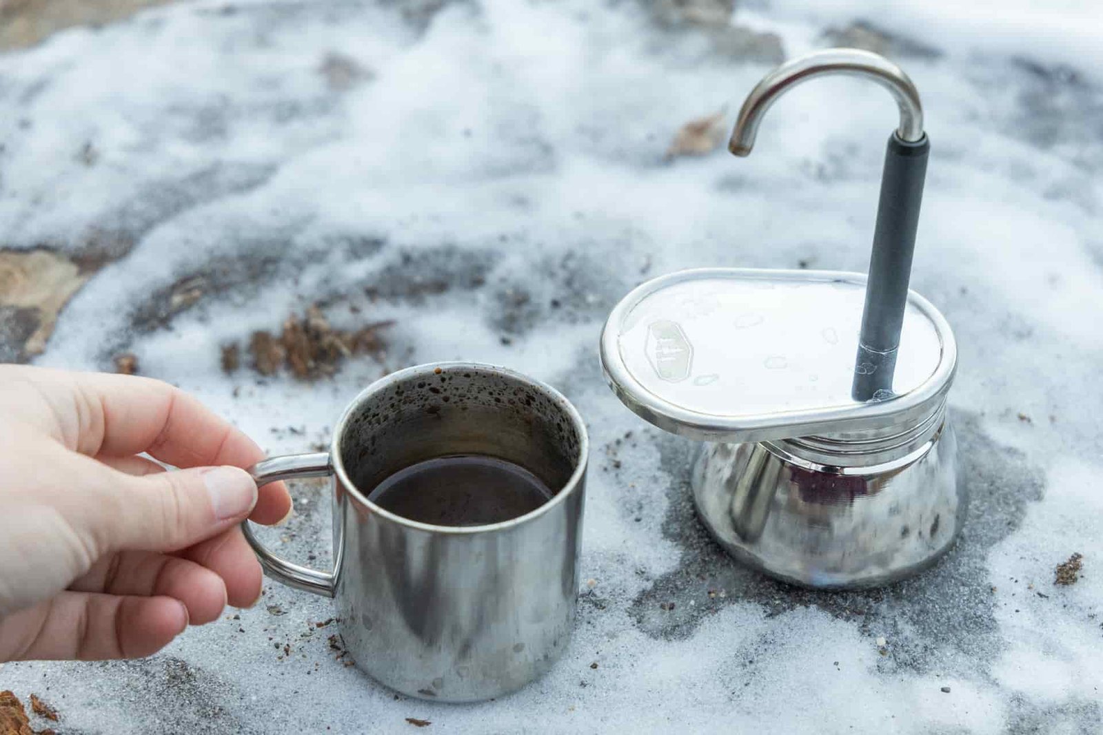 A hand grabs the small cup full of coffee from next to the GSI Mini Espresso.
