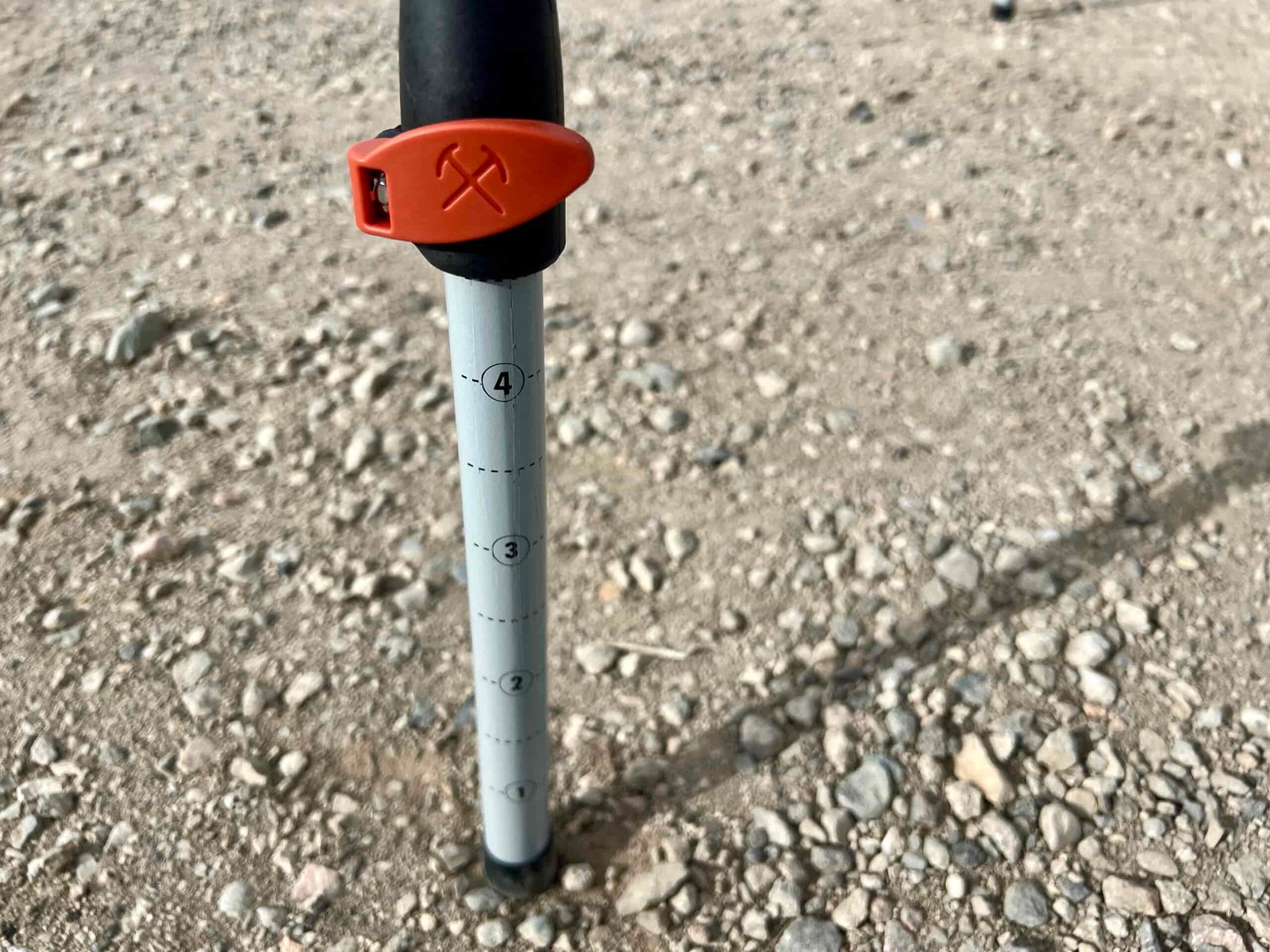 Close-up of the REI Camp Prep Table's adjustable legs. It has an orange lever lock. The leg is standing on gravel.