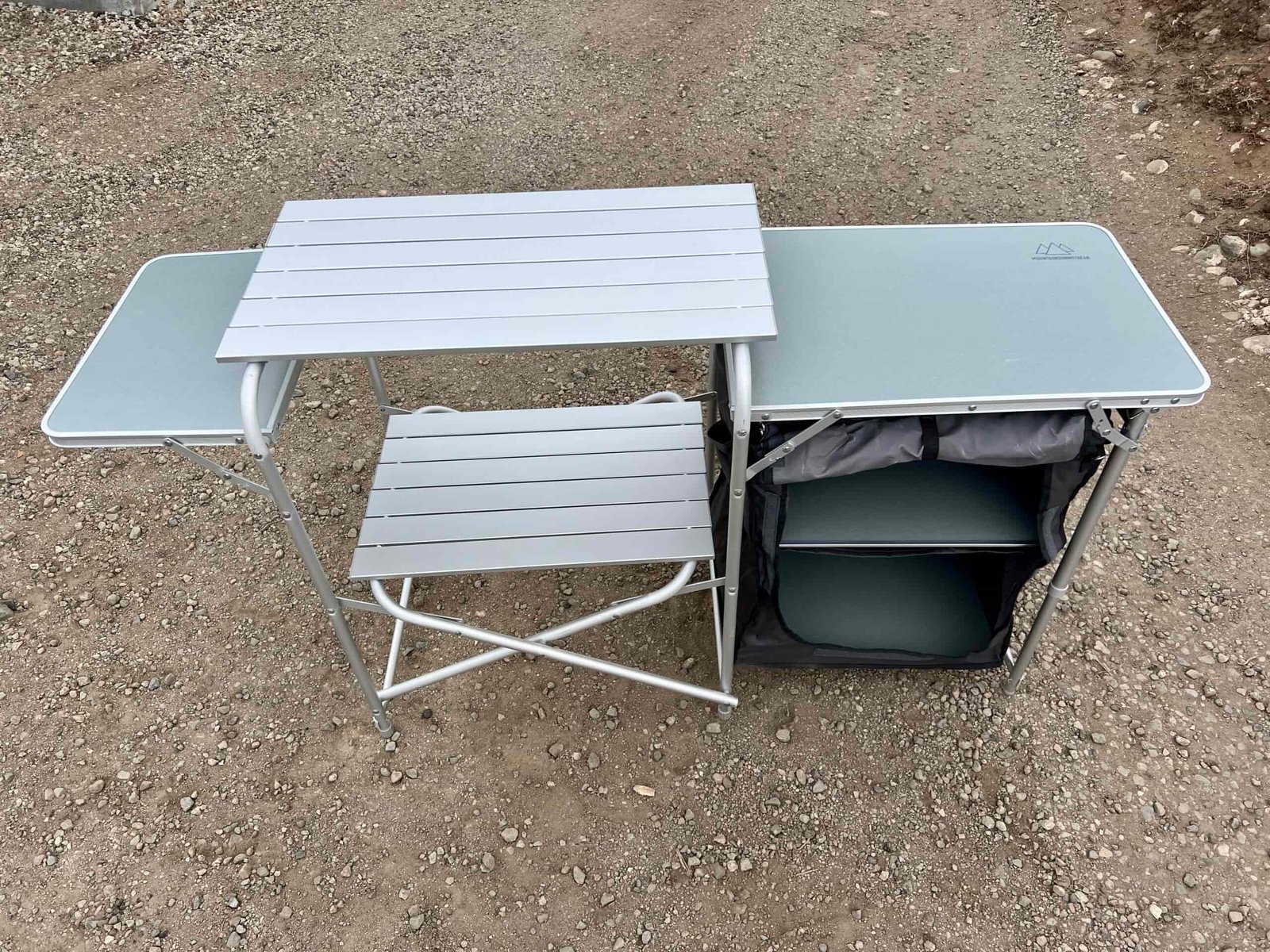 The Mountain Summit Gear Deluxe Roll Top Kitchen stands empty on gravel.