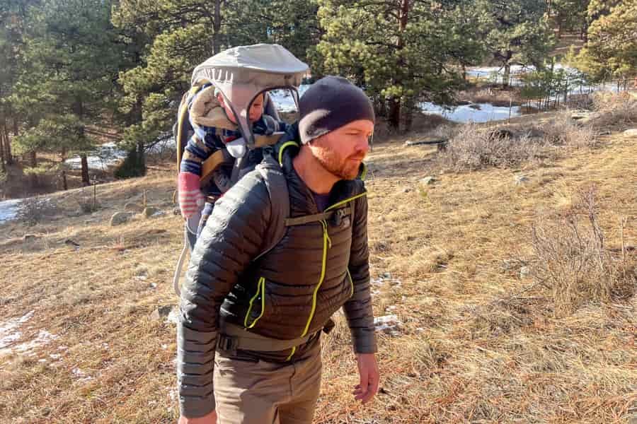 Parent hiking with a child seated in the Kelty PerfectFIT Journey Elite carrier on a grassy trail.
