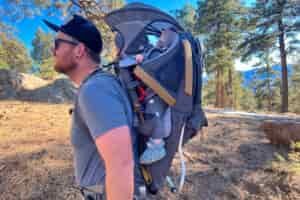 A close-up of a child's foot secured in a stirrup strap of a baby backpack carrier, providing support and comfort during hikes.
