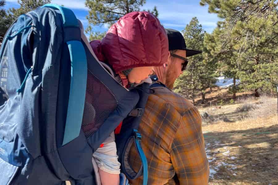 Side profile of a parent carrying a child in the Kelty PerfectFIT Journey Signature carrier during a hike.
