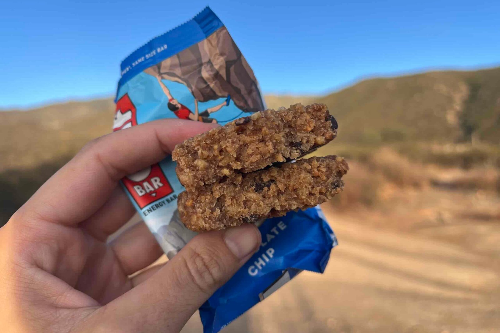 hand holding up Clif Bar in a mountainous setting