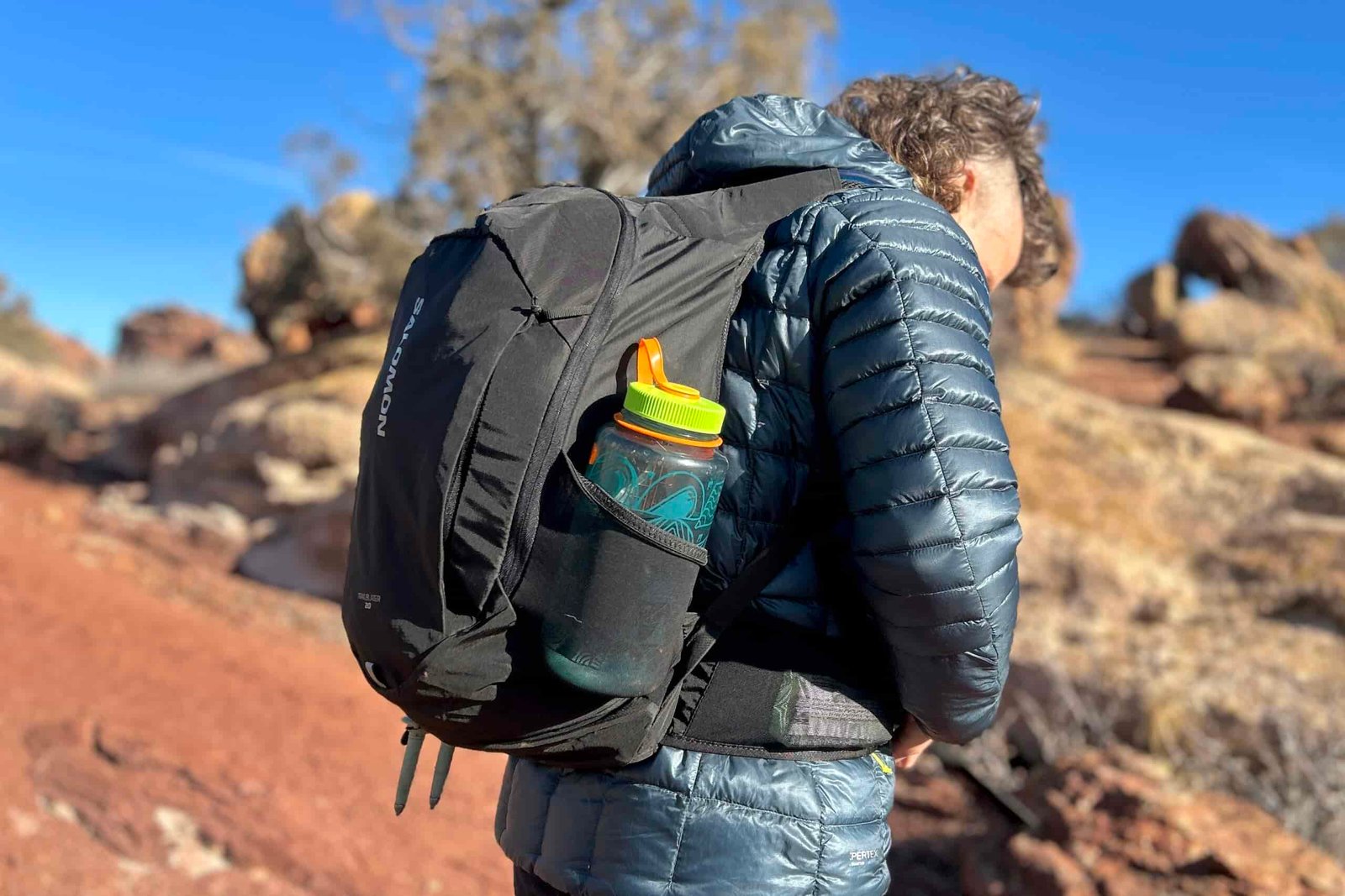 Close-up image from behind of a man adjusting a daypack, showing off the profile of the bag.