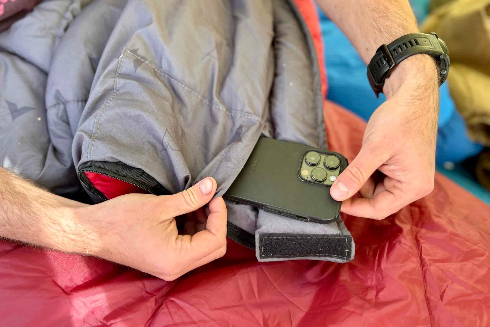Close-up image of a person pulling a phone out of an internal stash pocket of a sleeping bag.