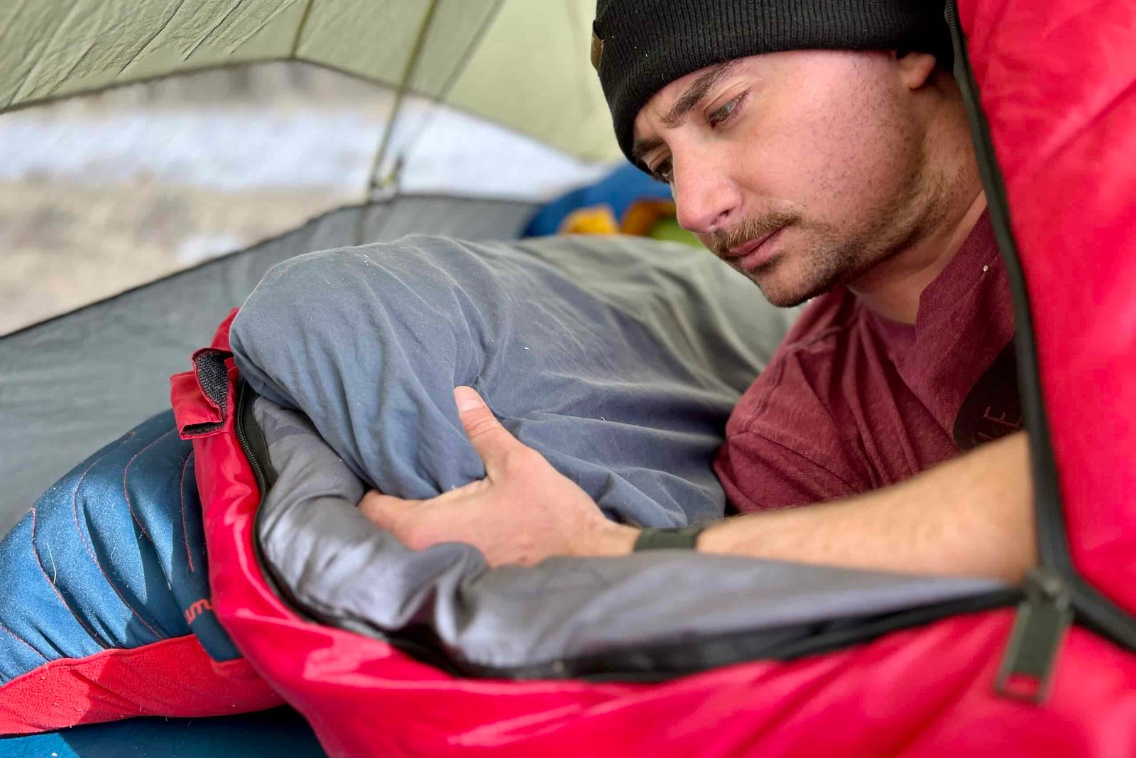 Close-up image of a man adjusting a pillow while inside a sleeping bag.