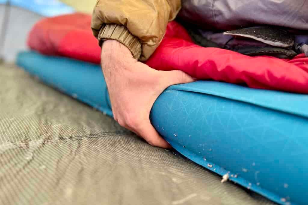 A hand grasps the side of a thick camping mattress.