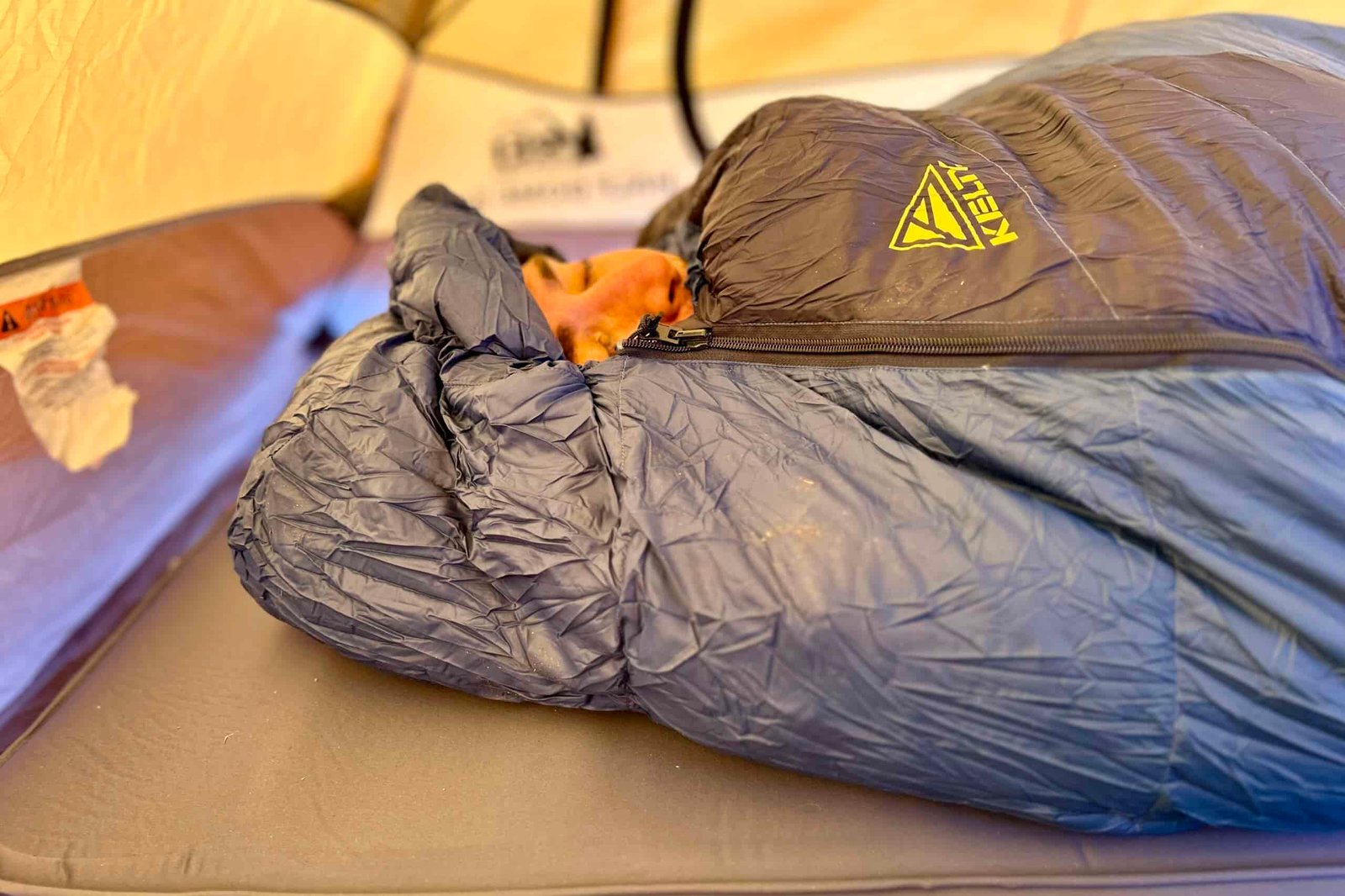 Close-up shot of a person inside a sleeping bag with the mummy hood tightened around their face and the zipper pulled to the top.