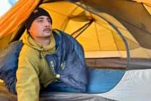 A man looks out of a tent to take in the view while still in his sleeping bag.