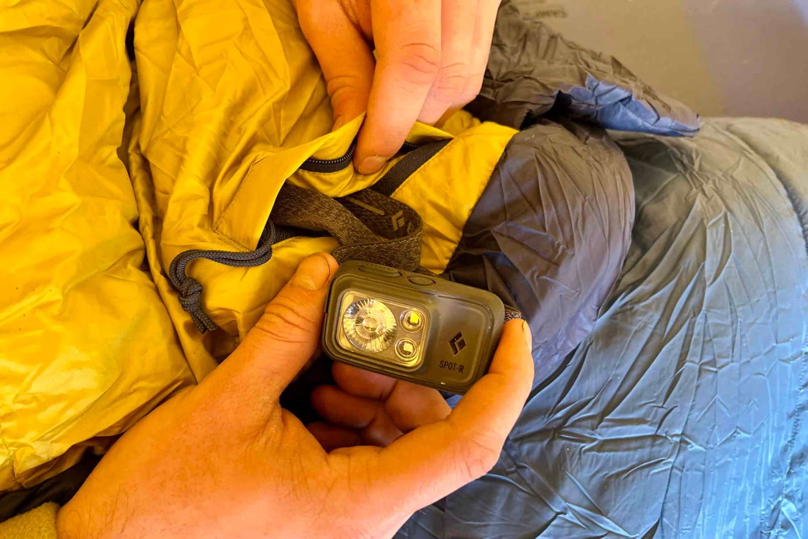 Close-up shot of two hands pulling a headlamp out of a sleeping bag's zippered internal stash pocket.