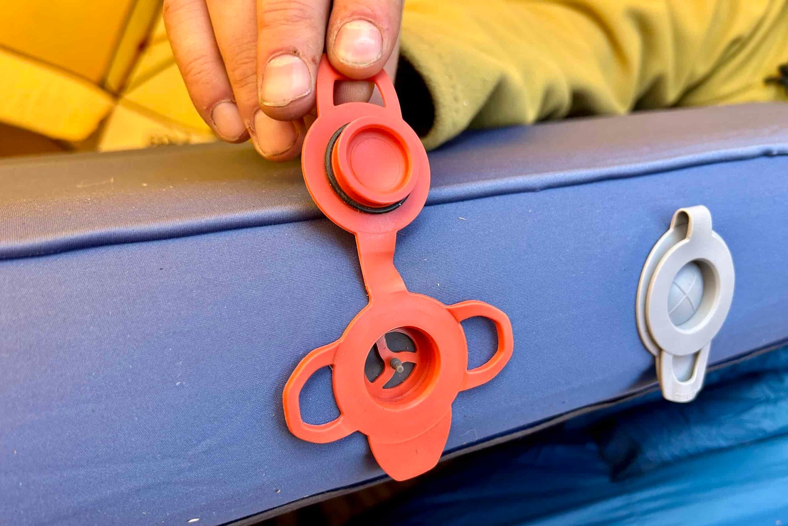Close-up image of an intake and dump valve on a camping mattress. A hand holds open the intake valve.