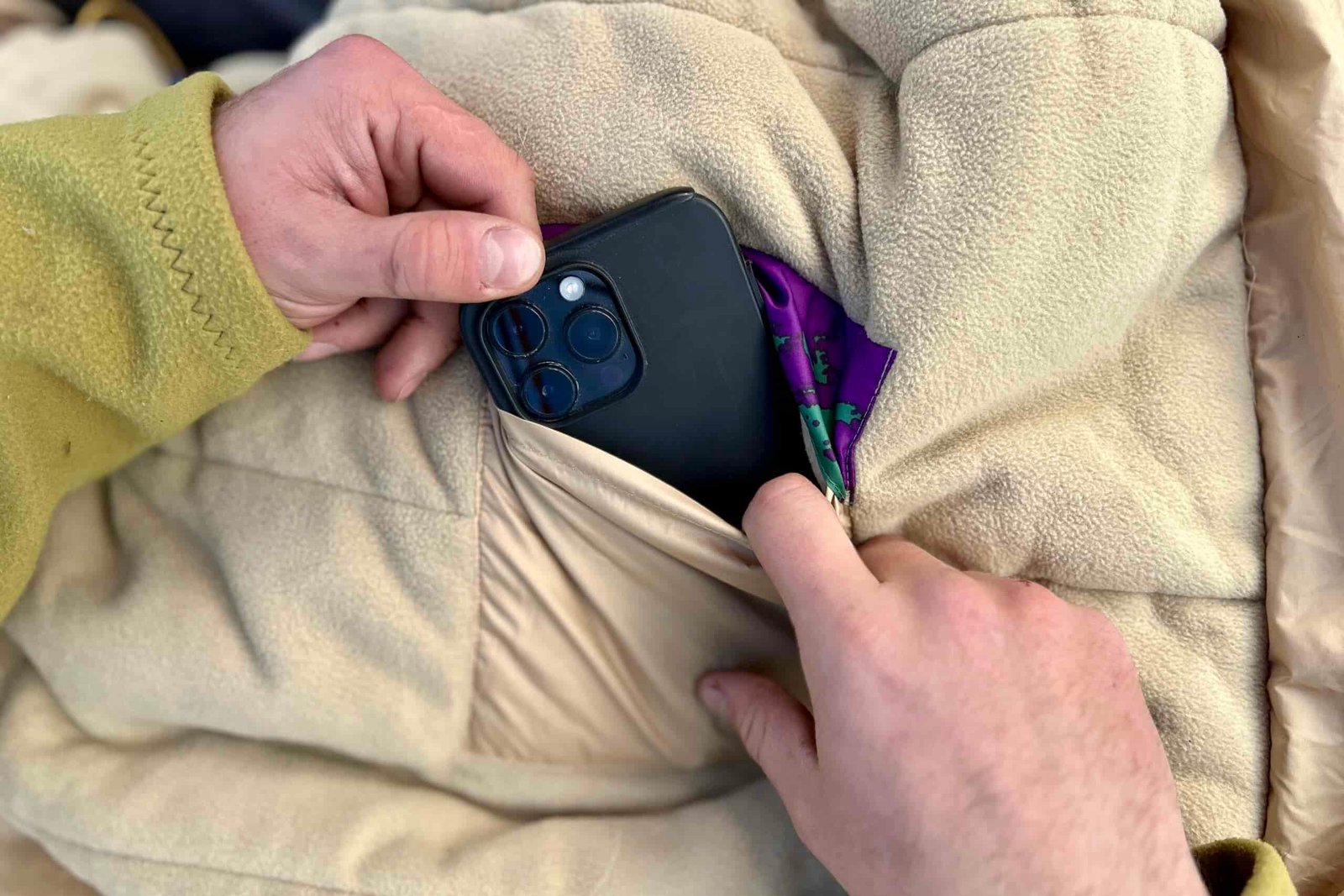 Close up image of a person's hands pulling a phone out of an internal sleeping bag pocket.