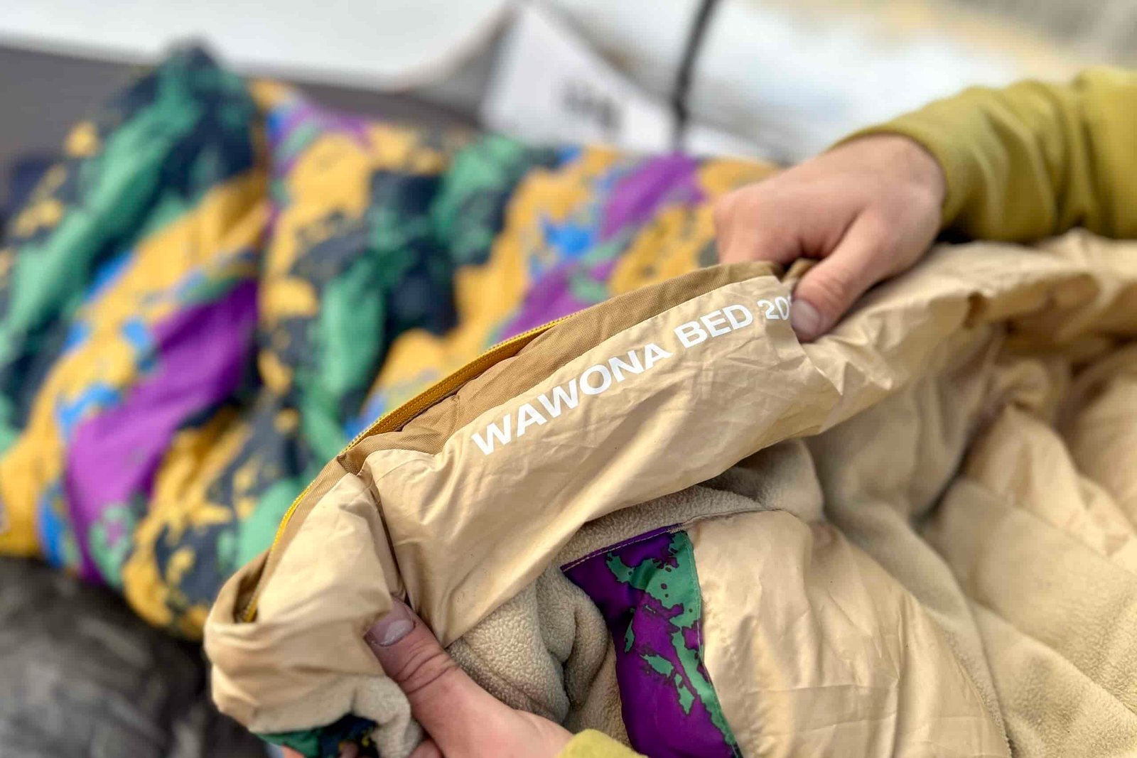 Close up shot of two hands holding onto the collar draft tube of a sleeping bag with the words "WAWONA BED 20" printed on the inside.