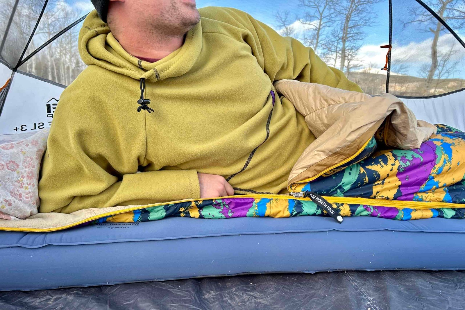 Close up image of a man in a sleeping bag in a tent leaning on one arm and sitting up slightly.