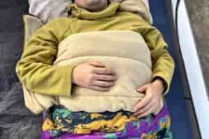Close up image from above of a person laying in a sleeping bag with the edge folded down like a blanket, and their arms on top.
