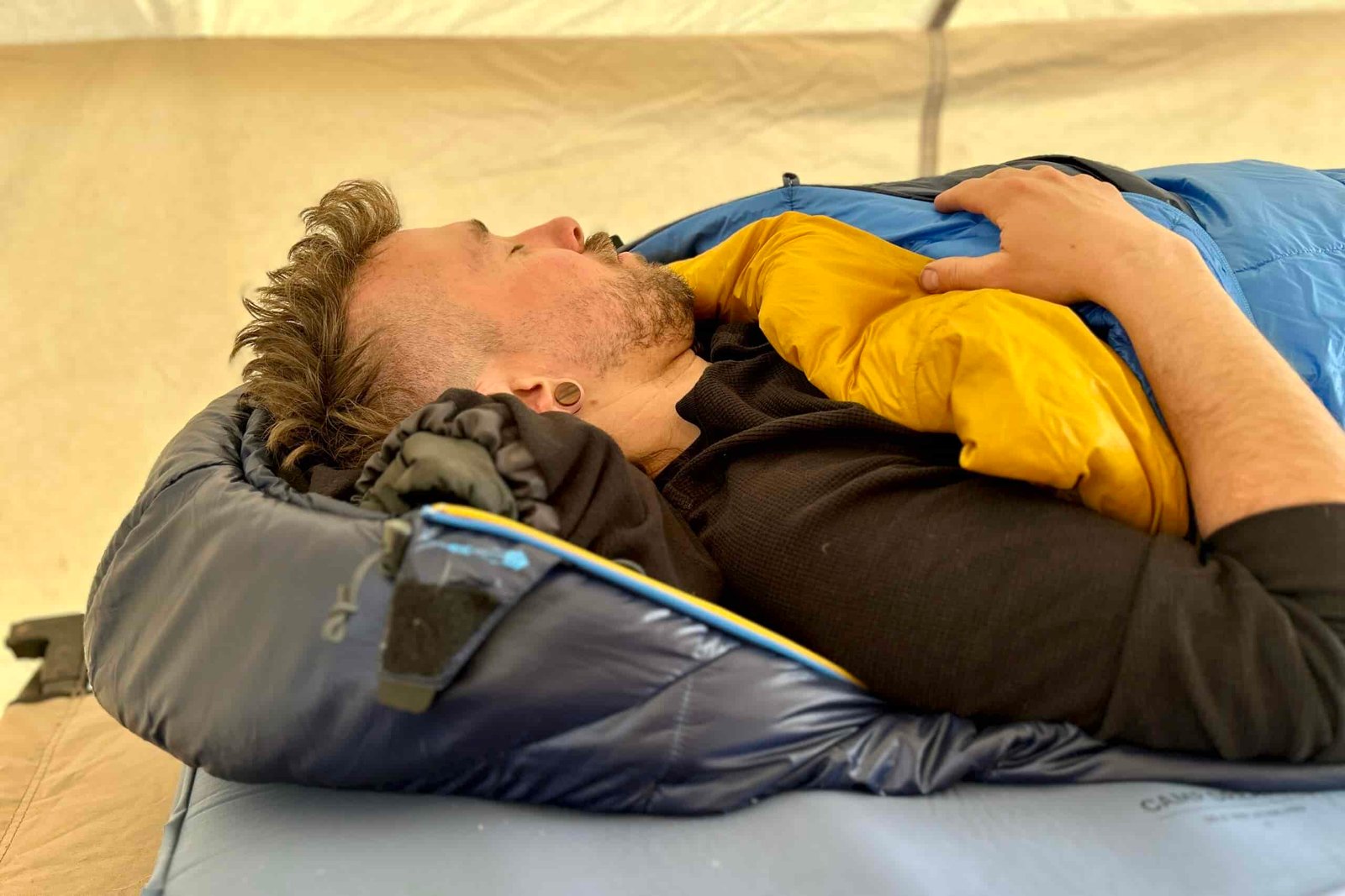 Close-up side image of a man resting in a sleeping bag in a tent with one arm out.