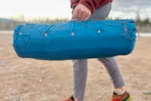 Close-up image of a person walking with a packaged camping mattress at their side.