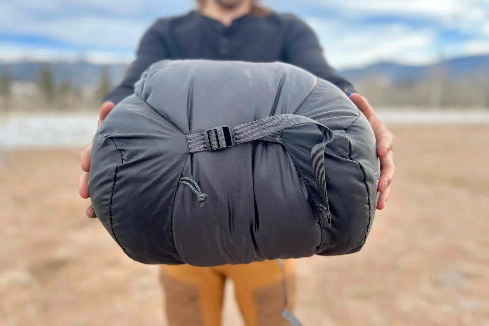 Close-up image of a person holding a sleeping bag in a stuff sack.