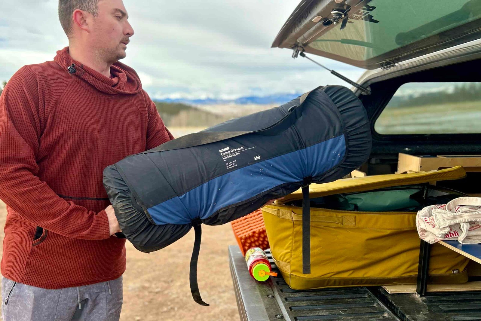 A man loads a rolled-up sleeping mattress into the back of a truck.