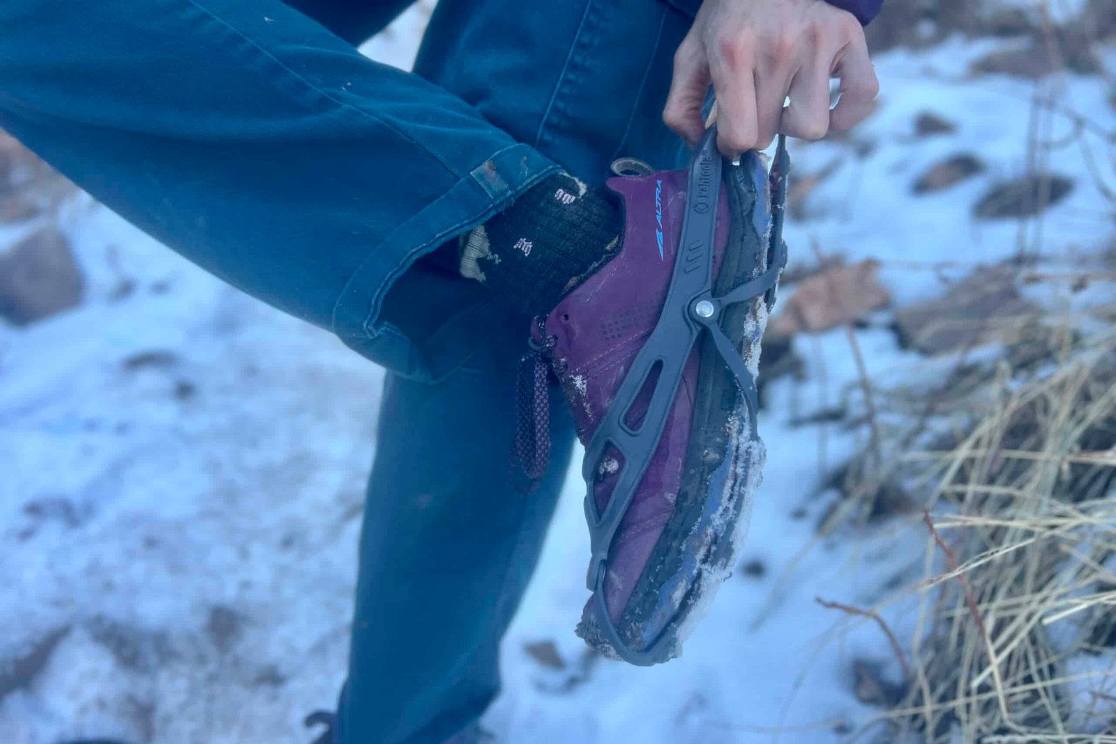 A hiker pulls a pair of ice cleats onto their feet against a snowy background.