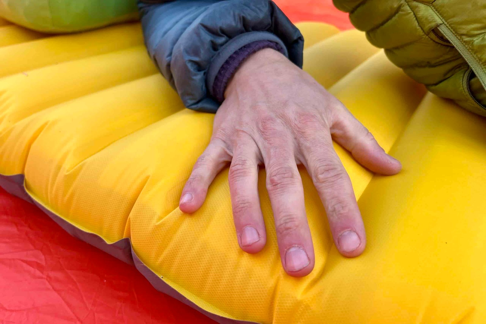Close-up image of a person's hand resting on the thick baffles of a sleeping pad.