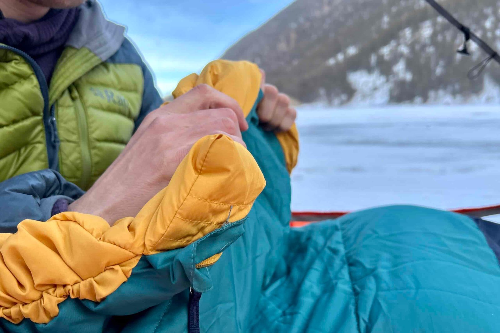 Close up image of a person holding the draft tube at the neck of a sleeping bag in a wintry setting.