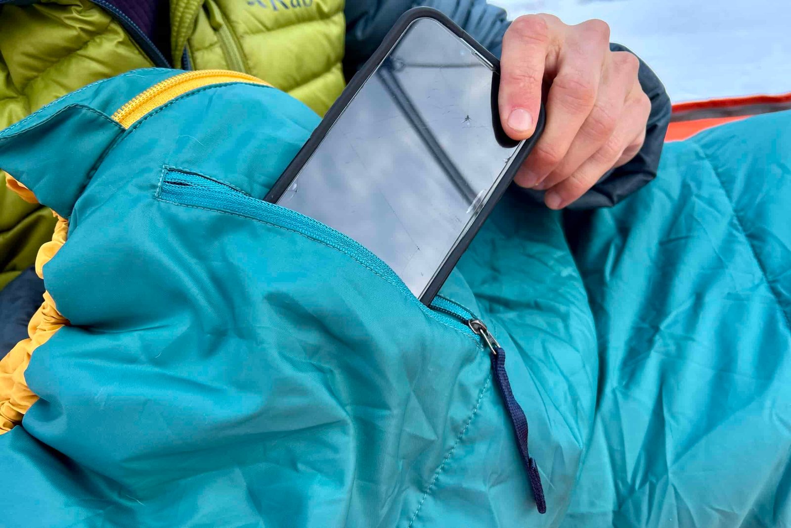 Close up image of a person putting a phone into a zippered stash pocket of a sleeping bag.