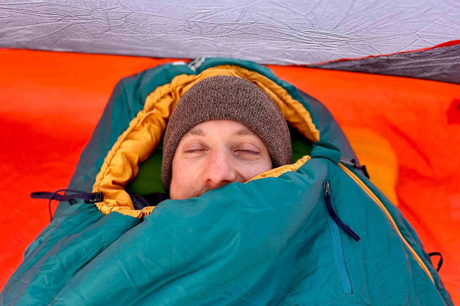 Close up image of a man from above in a sleeping bag with the hood pulled underneath his chin.