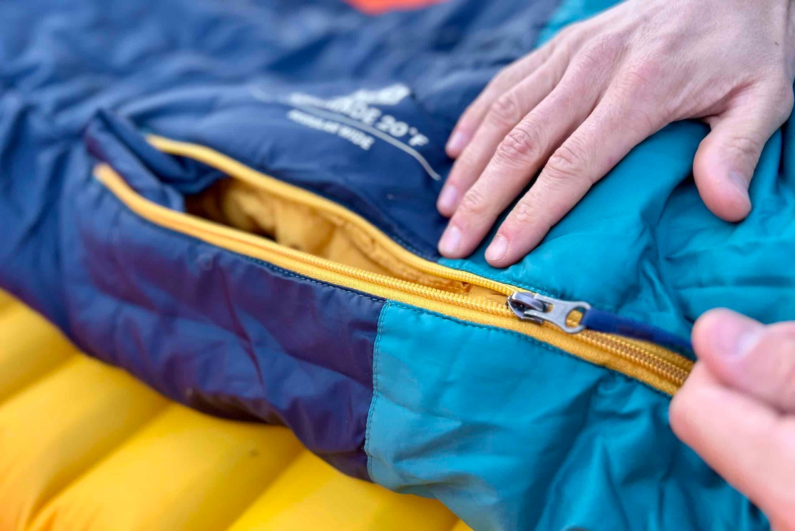 Close up image of a person's hand pulling the zipper tab of a sleeping bag.