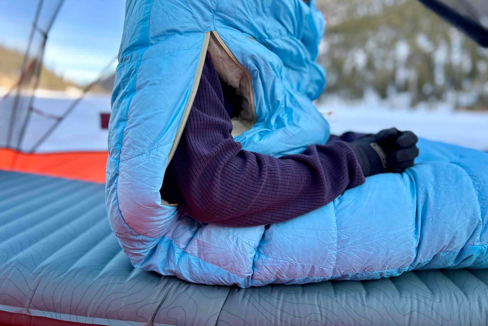 Close up image of a person sitting up in a sleeping bag with his arms sticking out of arm holes.