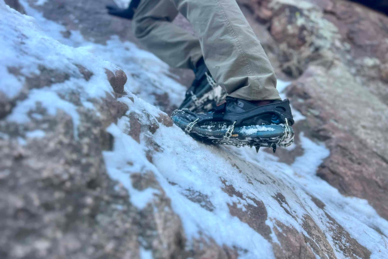 A foot scales an icy rock face with a pair of ice spikes.